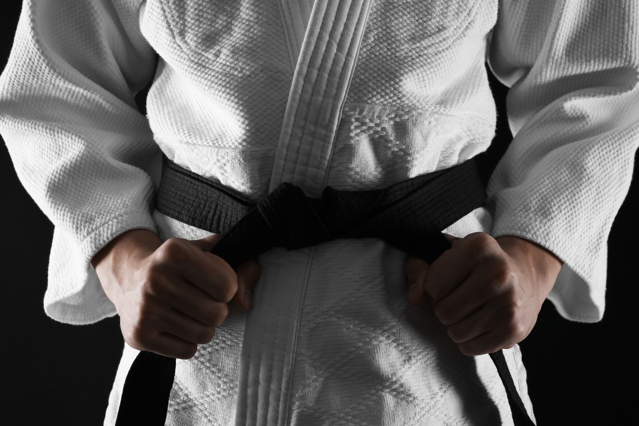 Man in Keikogi Tying Black Belt on Dark Background, Closeup. Mar